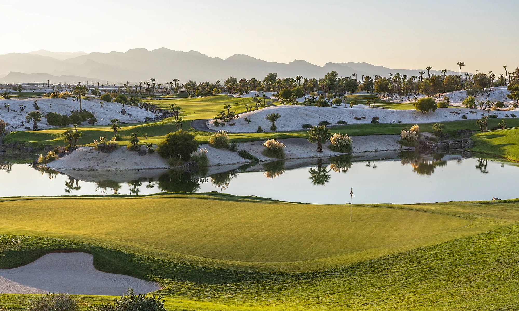 Sunlit desert golf course with a lake and mountains in the distance